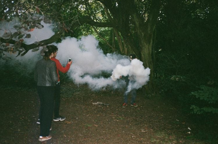 photo of two people in the forest looking at some white smoke